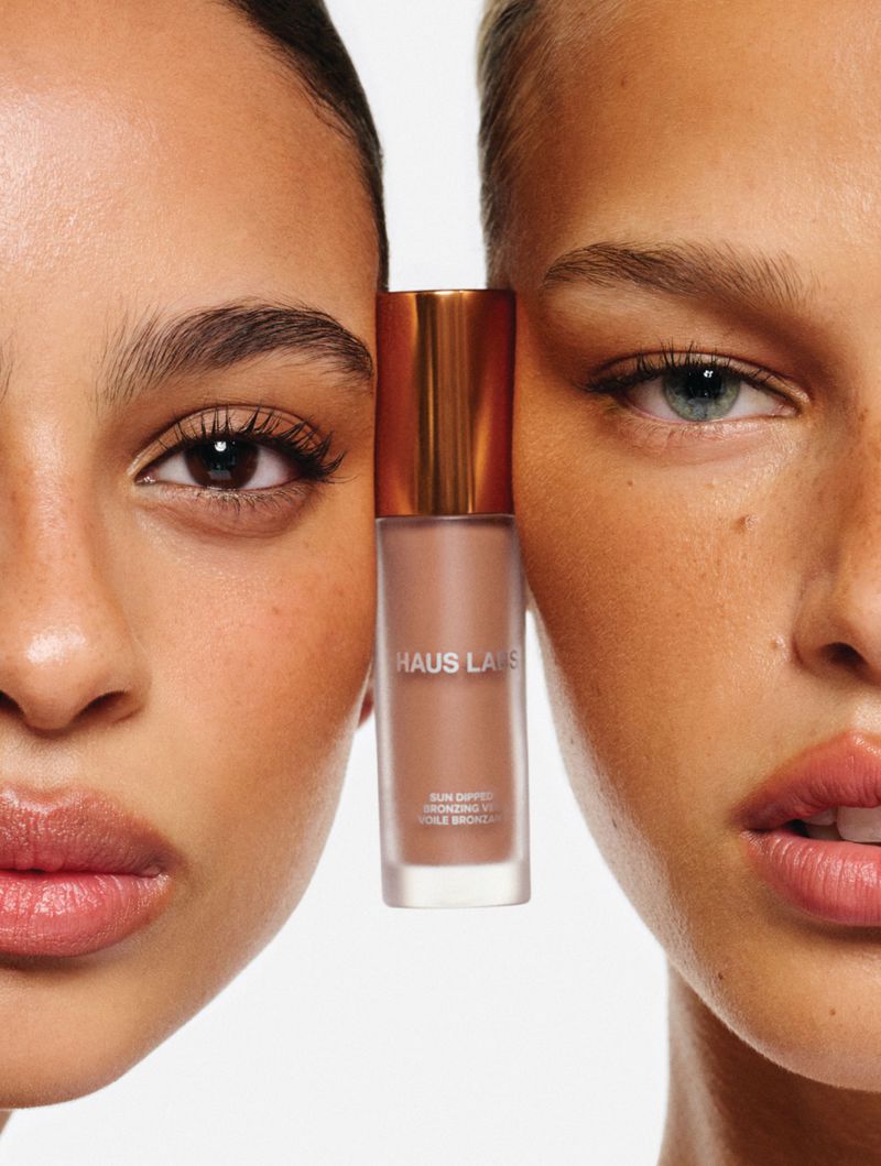 Two models framing a bronzer bottle by Haus Labs against a clean white background