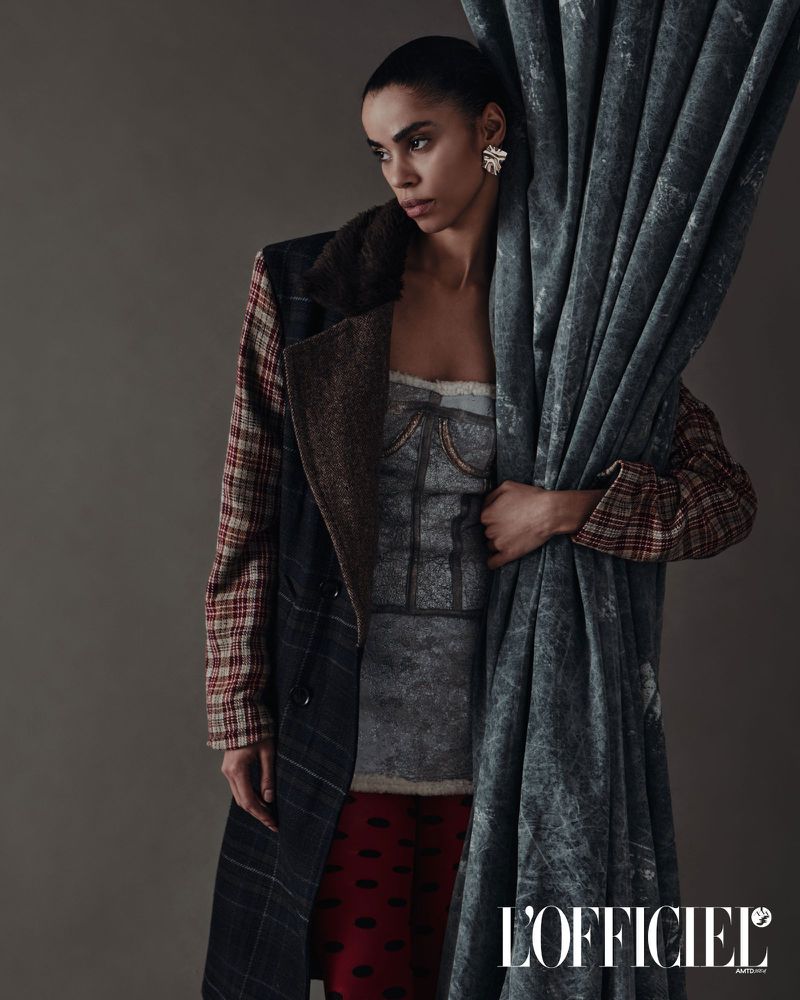 Fashion editorial shot of a woman in a coat and corset top, holding a curtain in a studio setting, with the L'Officiel logo visible.