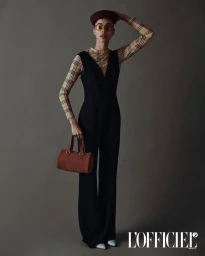Model wearing a black jumpsuit over a plaid top holding a brown handbag against a grey backdrop for L'Officiel Ukraine