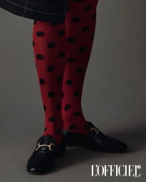 Close-up of model's legs wearing red polka dot tights and black leather loafers against a dark grey background.