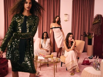 Group of four models in elegant attire posing in a luxurious pink room with velvet curtains for Saks Fifth Avenue.