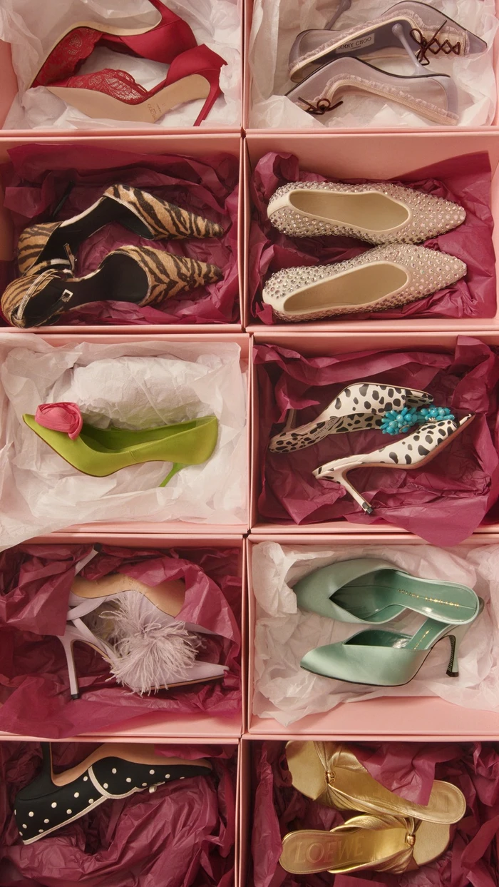 An assortment of designer high heels and mules displayed inside pink shoeboxes lined with tissue paper.
