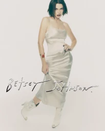 Julia Fox wearing a silver satin slip dress and white boots against a white studio background for Betsey Johnson Holiday 2026