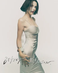 Julia Fox wearing a sleek cream slip dress for the Betsey Johnson Holiday 2026 campaign against a plain white background.