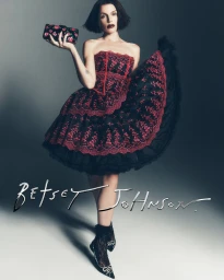 Julia Fox in a red and black lace dress holding a floral clutch for Betsey Johnson Holiday 2026 campaign.