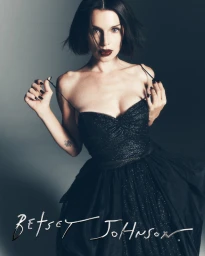 Julia Fox wearing a black strapless dress against a grey studio seamless backdrop for the Betsey Johnson Holiday 2026 campaign.