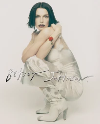 Julia Fox crouching in a glossy white dress and embellished boots for the Betsey Johnson Holiday 2026 campaign.