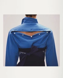 Rear view of a person wearing a vibrant blue button-up shirt featuring an inverted back yoke and white buttons against a plain white background.