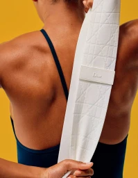 Close-up back view of a person wearing a navy tank top, holding a white textured Dior fitness band against a yellow background.
