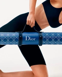 Woman in activewear holding a branded blue Dior yoga mat against a white background