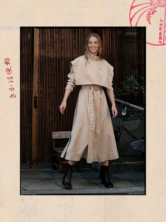 Model in a beige trench coat posing outdoors in front of a wooden slatted door and bicycle for Banana Republic