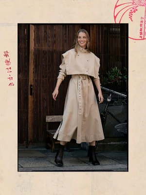 Model in a beige trench coat posing outdoors in front of a wooden slatted door and bicycle for Banana Republic