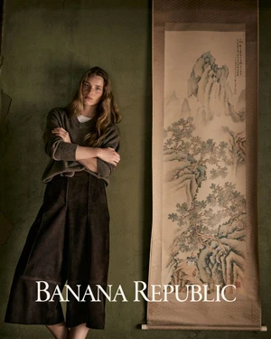 Model standing with arms crossed next to a hanging scroll against an olive green wall for Banana Republic