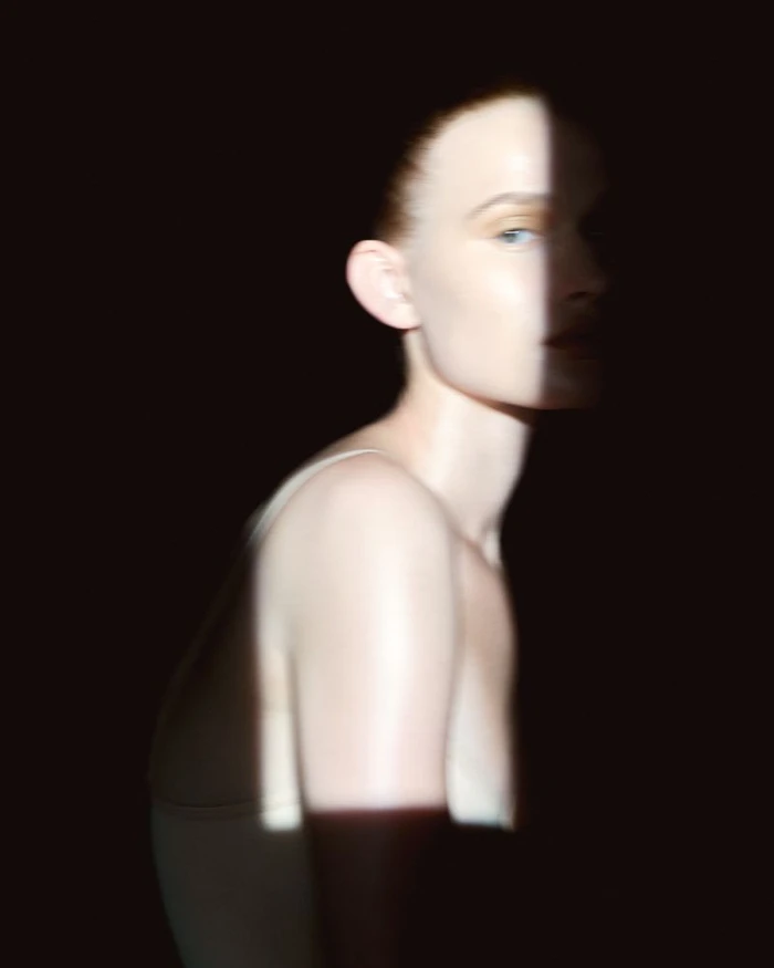 Close-up portrait of a woman with a vertical sliver of light illuminating her face and shoulder against a dark background