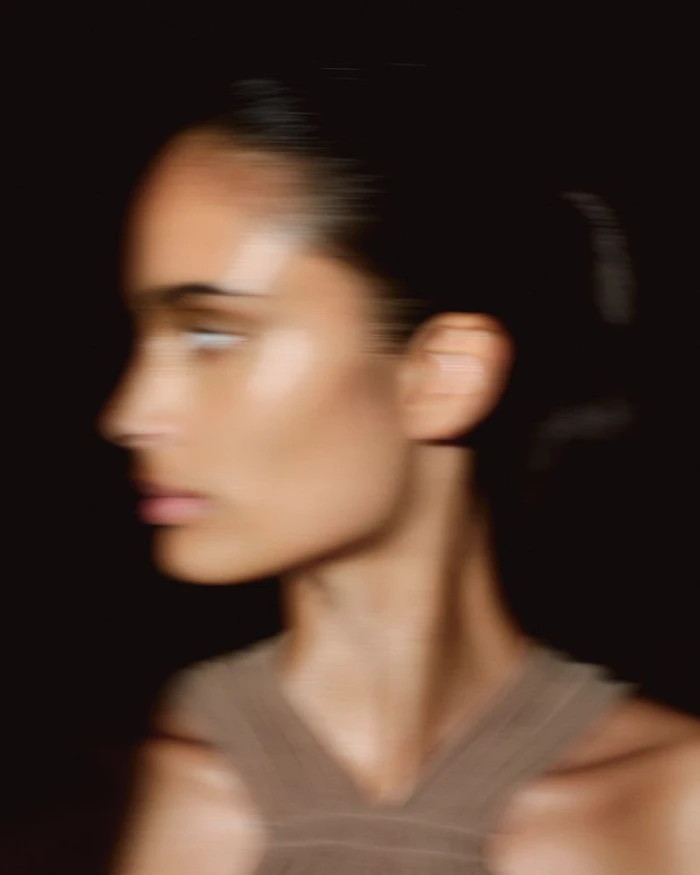 Motion blurred profile portrait of a model with glowing skin wearing a brown halter top against a black background