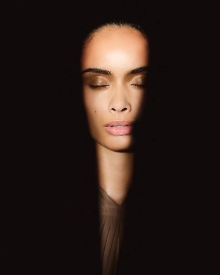 Close-up portrait of a woman with closed eyes illuminated by a soft light beam against a dark background for Skin Veil Ellis Faas Fall 2026.