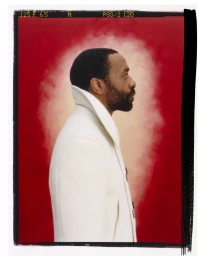 Profile portrait of Chiwetel Ejiofor wearing a white coat against a vibrant red backdrop with white smoke effect.