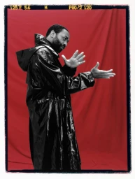 Chiwetel Ejiofor wearing a black glossy trench coat gesturing against a vibrant red backdrop for Esquire UK