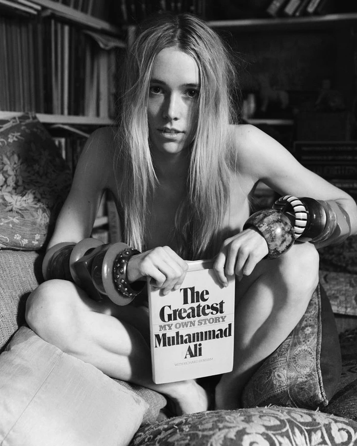 Black and white portrait of a woman seated holding a book by Muhammad Ali wearing large bracelets