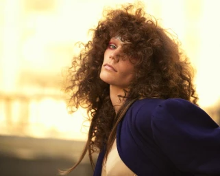 Model with voluminous curly brown hair and a blue jacket posing outdoors for System Magazine.