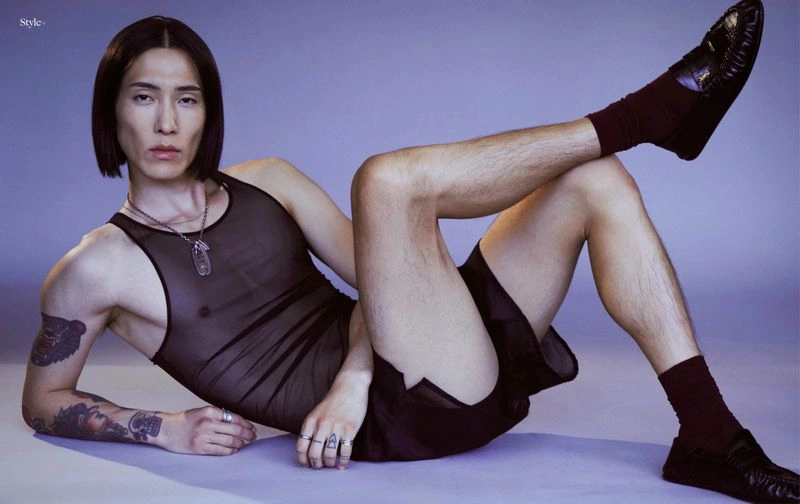 Model Hyuk Kim lying down on a purple seamless backdrop wearing a black sheer tank top and dark shorts