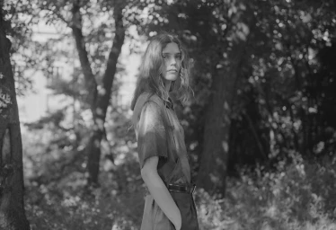 Black and white portrait of a person with long hair standing among trees outdoors for Crosscurrent.