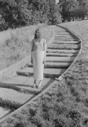 Model wearing a striped t-shirt and a stiff cylindrical skirt standing on an outdoor stone staircase.