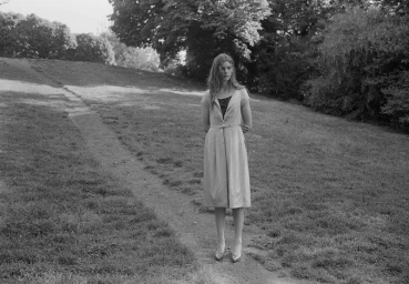 Woman in midi dress standing on a grassy path in a park shot by Mark Steinmetz