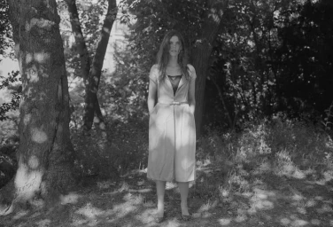 Monochrome portrait of a woman standing outdoors in a wooded area wearing a buttoned midi dress for Crosscurrent Another Way.