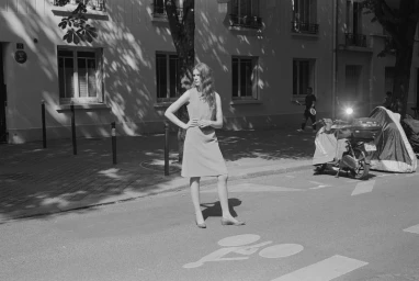 Model standing on a city street in a sleeveless dress with a scooter parked nearby in monochrome
