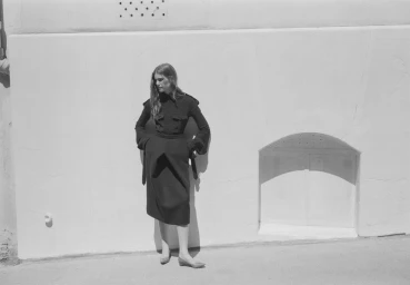 Model standing against a light stucco wall wearing a dark long-sleeve top and midi skirt for Another Way by Crosscurrent