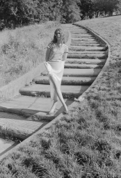 Model wearing a striped t-shirt and light skirt standing on curved outdoor concrete steps flanked by grassy banks.