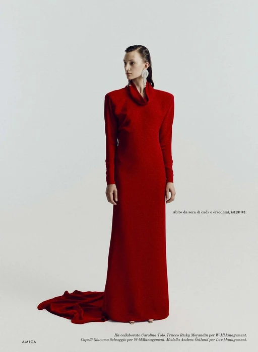 Model Andrea Ostlund wearing a long red gown with structured shoulders against a neutral studio background for Amica magazine.