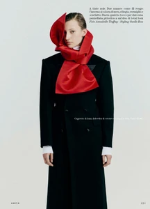 Model wearing a structured black coat with a voluminous red silk scarf wrapped around her head and neck against a plain background.