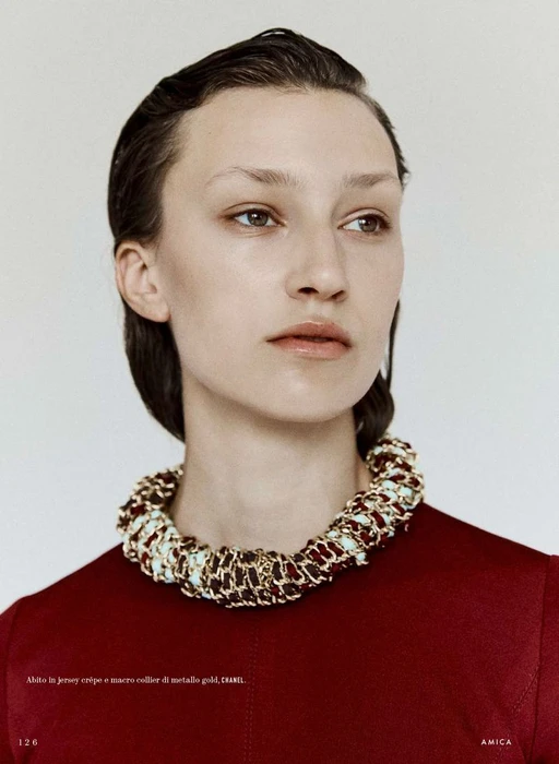 Portrait of a woman wearing a red top and a chunky woven necklace against a neutral background