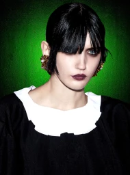 Portrait of a woman with dark hair and fringe wearing a black top with white collar against a vibrant green background.