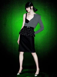 Model standing against a vibrant green gradient background wearing a grey cardigan and black skirt for N21 Nova project.