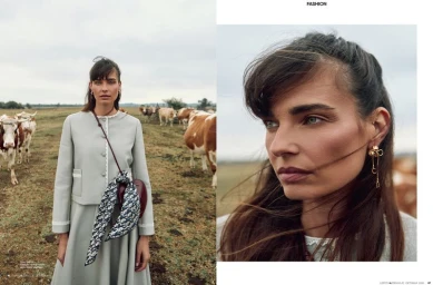 Model in a pale grey jacket and skirt standing outdoors in a pasture with cattle, photographed by Senja Vild.