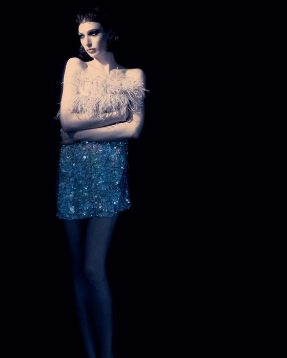 Model Brenda Pivatto wearing a feathered strapless dress and sequin skirt against a solid black background for Flanelle Magazine.