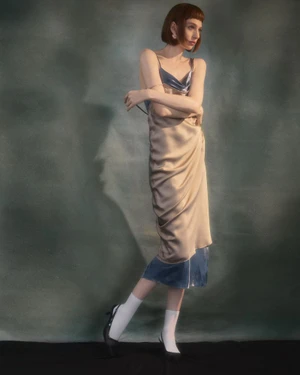 Model in a satin slip dress wearing white socks and dark shoes against a textured green and grey studio background