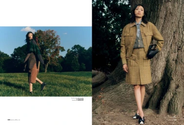 Model standing next to a large tree trunk wearing a tweed jacket and matching skirt holding a black handbag