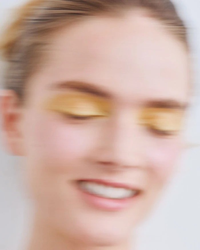 Close-up beauty portrait of a woman with yellow eyeshadow and motion blur against a white background