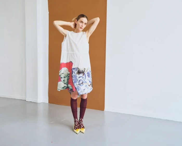 Model in a white printed dress and burgundy knee-high socks posing against a studio backdrop.