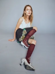 Model wearing a white top, printed skirt, and burgundy socks with high heels seated against a grey backdrop