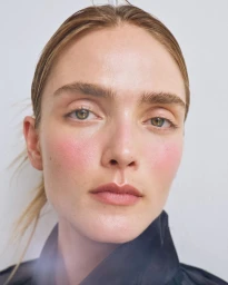 Close-up portrait of a woman with flushed pink cheeks and natural makeup against a plain white background