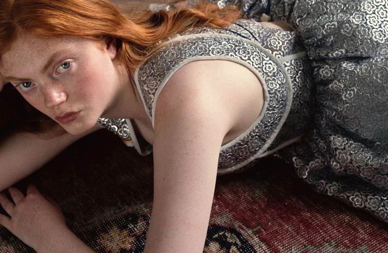 Red-haired female model lying on a patterned rug wearing a silver patterned dress for Heroine Magazine
