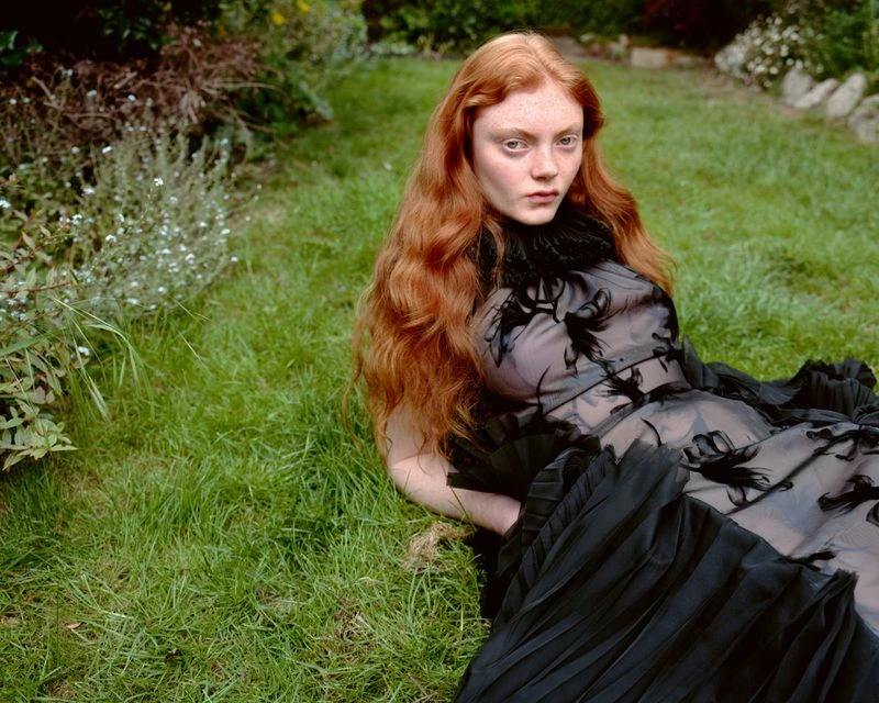 Red-haired female model lying on green grass wearing a black ruffled dress for Heroine Magazine editorial
