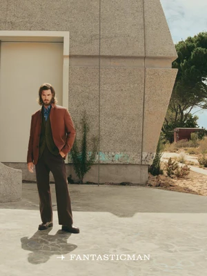 Andrew Garfield wearing a brown jacket standing outdoors near a brutalist concrete building for Fantastic Man China.
