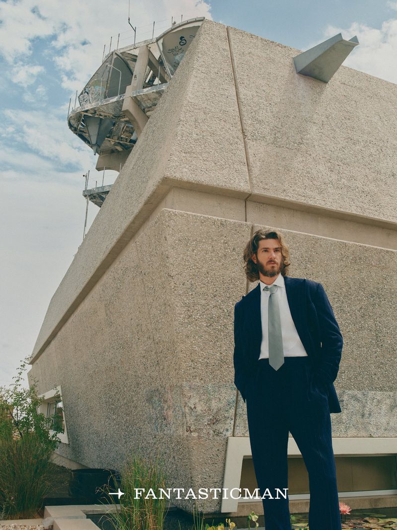 Andrew Garfield wearing a dark suit and tie standing outdoors in front of brutalist architecture for Fantastic Man China.