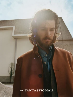Actor Andrew Garfield with long hair and beard wearing a brown jacket outdoors under bright sun flare for Fantastic Man China